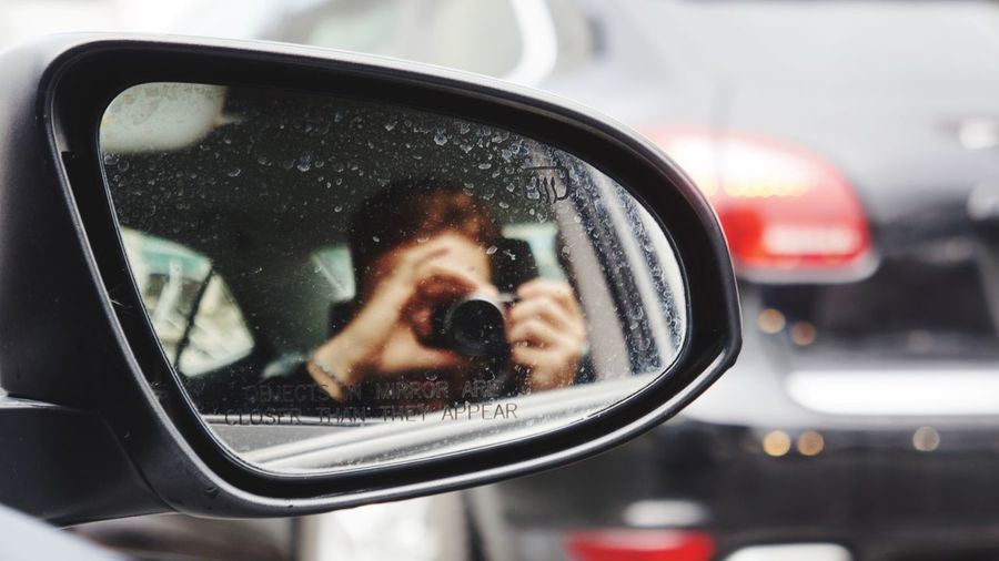 Reflection of man photographing car on side-view mirror