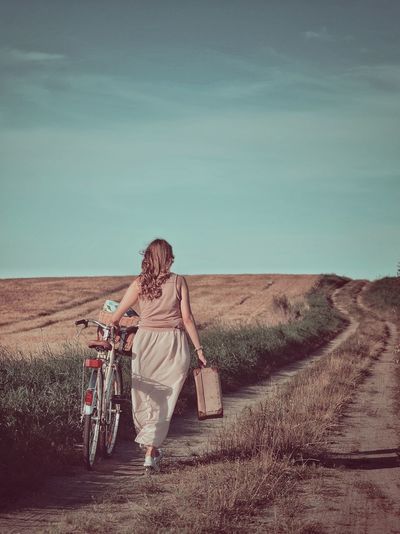 Rear view of woman walking with bicycle on field
