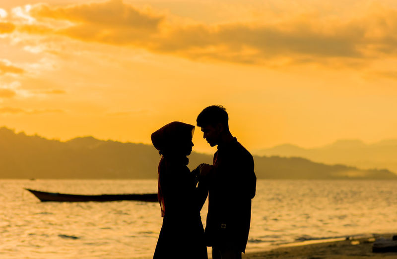 Silhouette woman standing at beach against sky during sunset