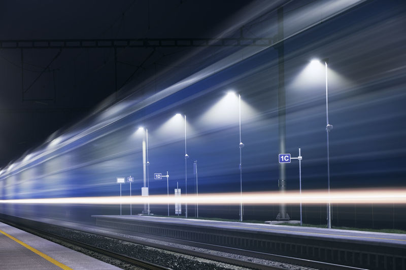 Railway at night. light trails of passenger train at illuminated railroad station.