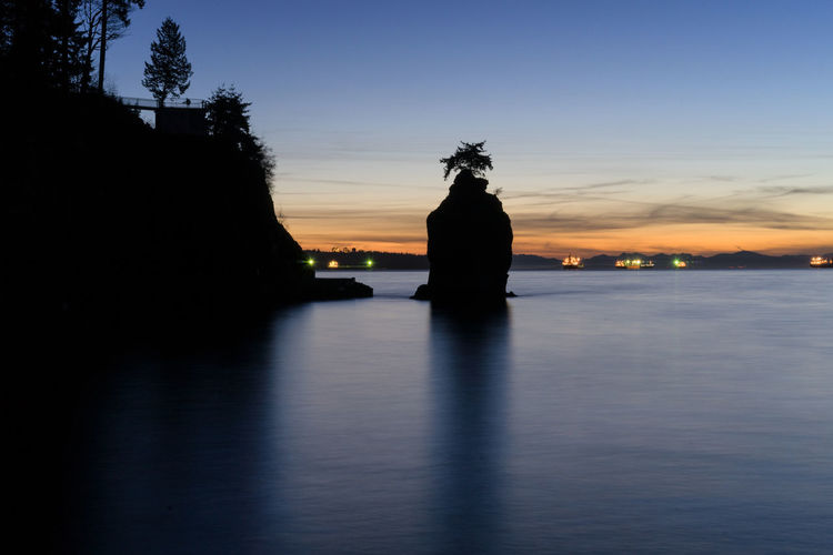 Silhouette rock formation in lake at stanley park against sky during sunset