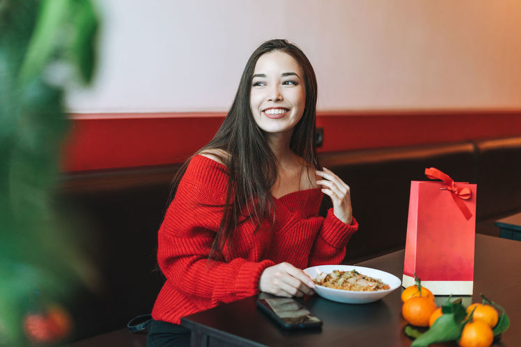 Beautiful smiling young asian woman in red clothes eating asian food in chinese  restaurant