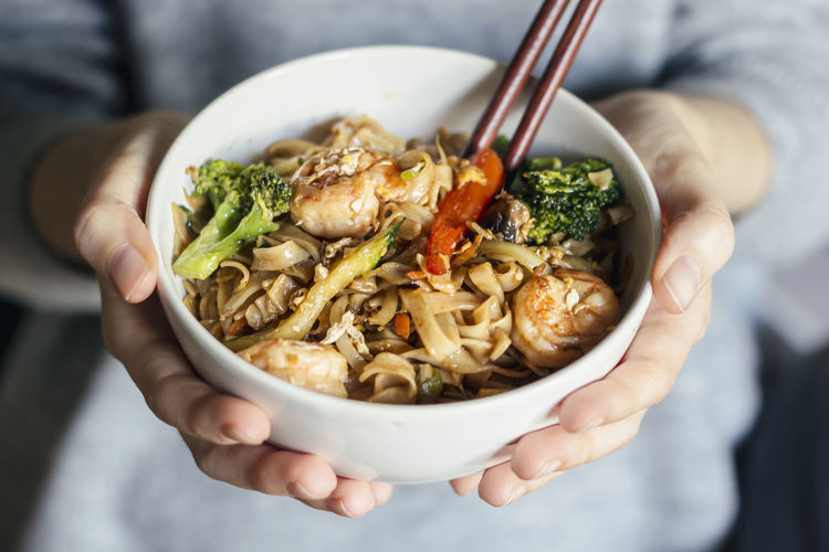Female holding a bowl of seafood thai noodles