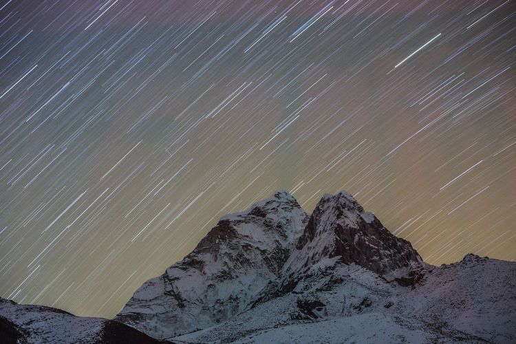 Star trails captured in a long exposure image of ama dablam in nepal.
