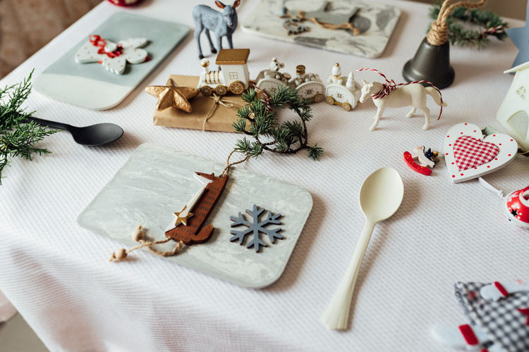 Top view composition with decorative snowflake and wooden fox figure hanging on pine tree branch arranged near spoon on table during christmas celebration