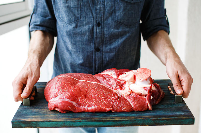 Man s hands holding rustic tray with beef piece, selective focus