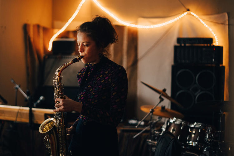 Young woman playing saxophone while rehearsing at illuminated studio