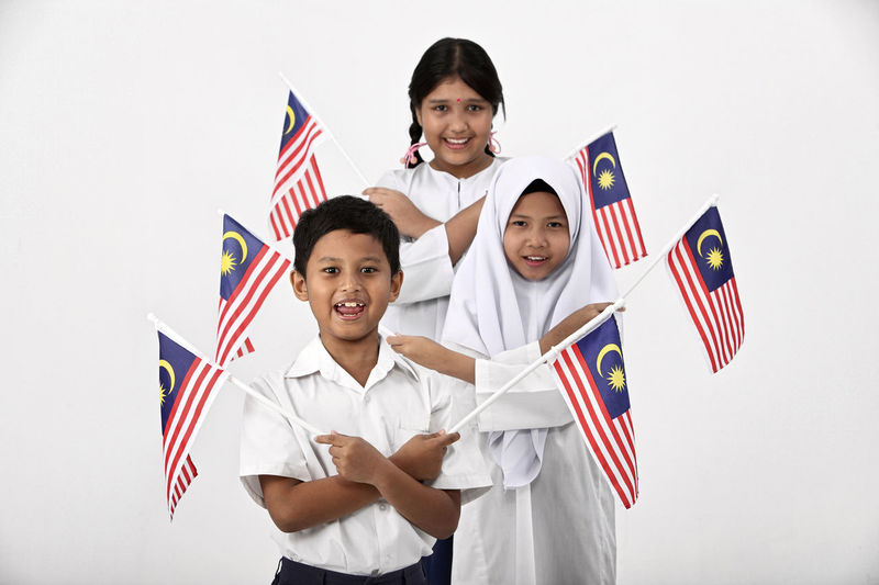 Portrait of smiling children with malaysian flags standing against white background