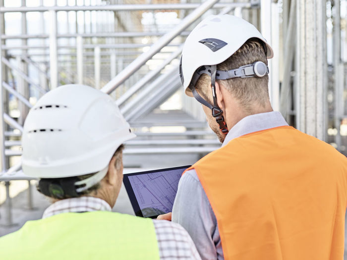 Architect and foreman with tablet wearing hards hat on construction site