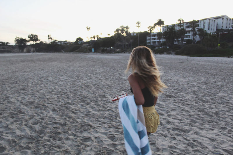 Woman carrying towel at beach during sunset