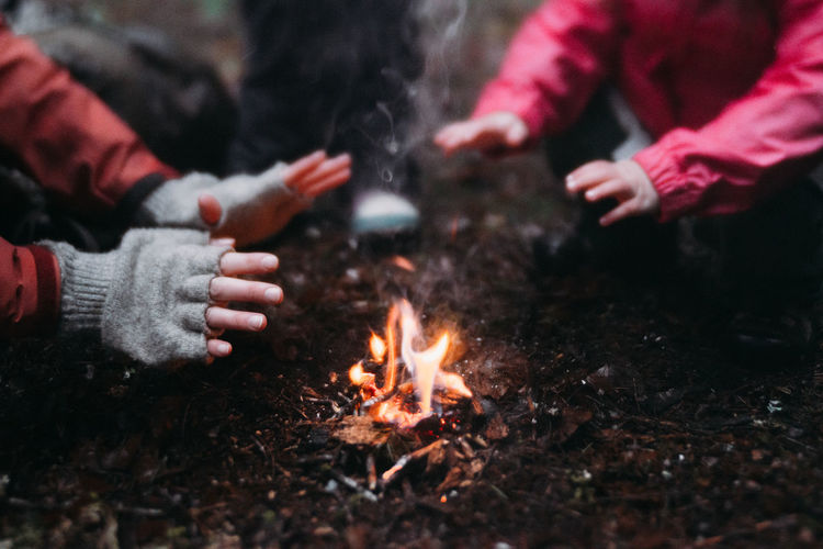 Cropped image of mother and daughter warming hands at campfire