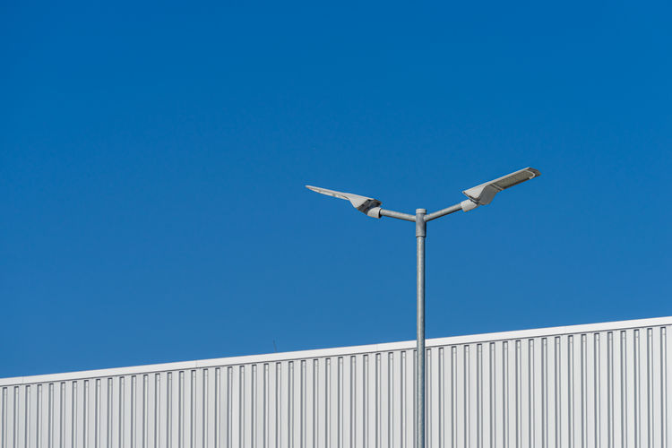 Low angle view of street light near warehouse against clear blue sky