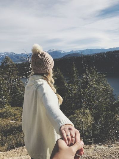 Cropped image of man holding hands with girlfriend against mountains