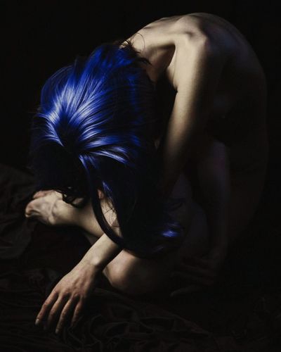 Naked woman with blue hair sitting against black background