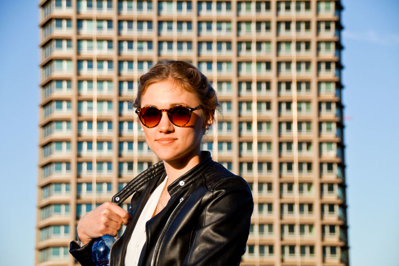 Portrait of young woman in sunglasses standing by building in city