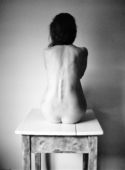 Rear view of shirtless woman sitting against wall