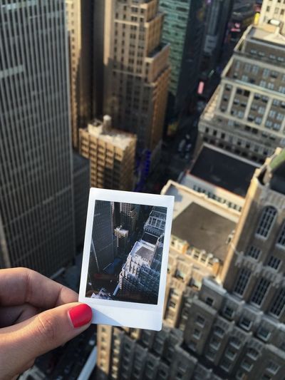 Close-up of female hand holding instant camera picture against buildings