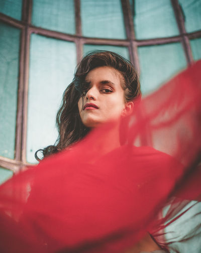 Low angle portrait of young woman wearing red dress against wall