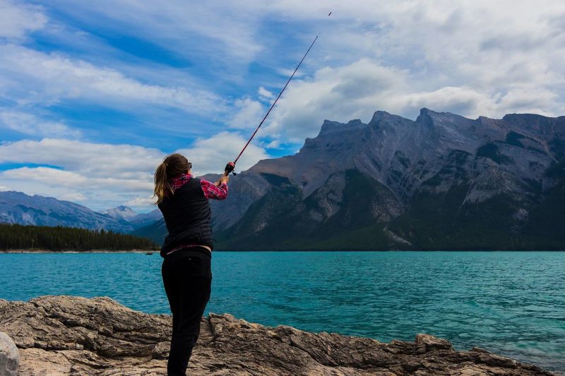 Woman fishing in lake against mountains