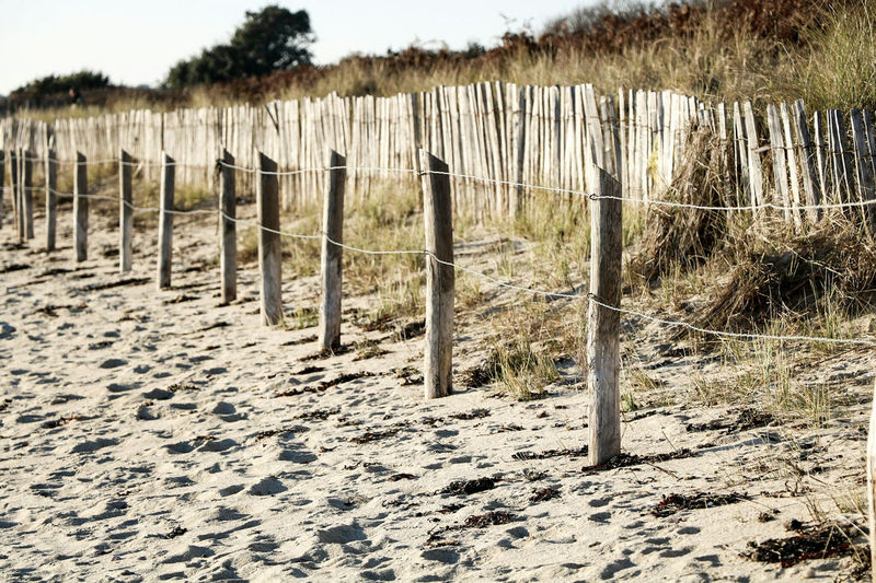 Wooden fence on sand against sky