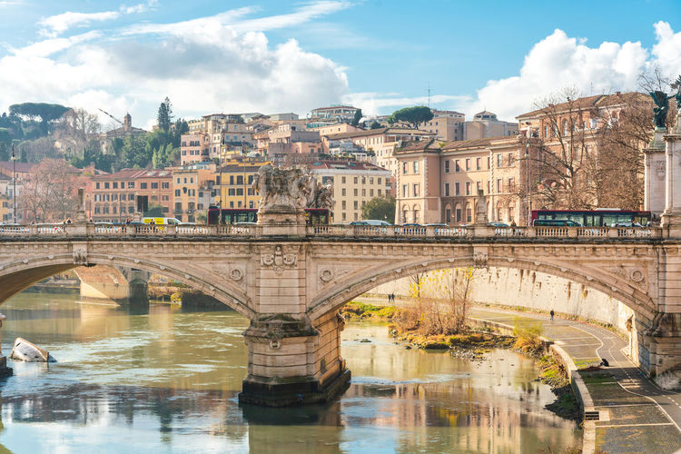 Bridge over river by buildings in city against sky