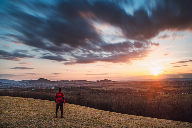 Man in a red and black shirt watching the sunset on an elevated spot in the czech republic.