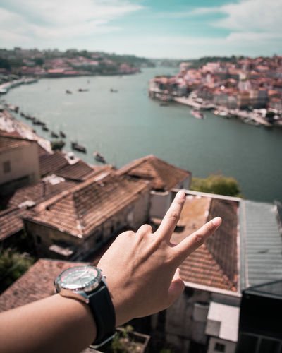 Cropped hand of person gesturing over houses and sea