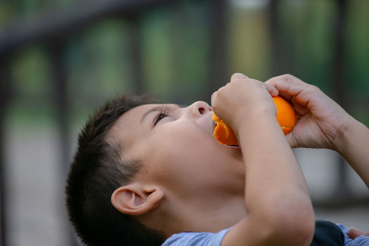 Boy squeezing orange juice in mouth outdoors