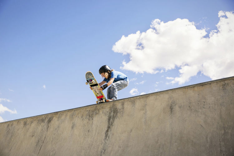 Low angle view of boy placing skateboard on ramp against blue sky