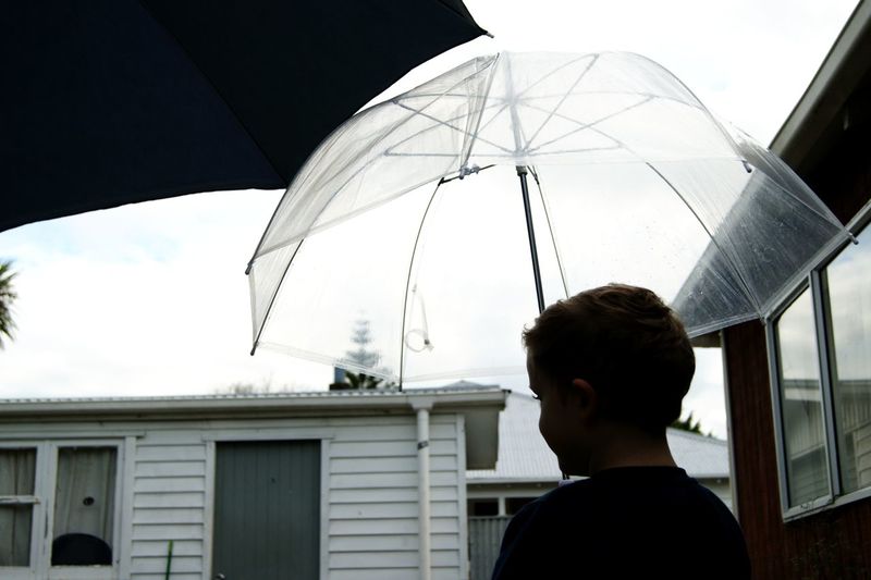 Rear view of boy holding umbrella while standing against houses