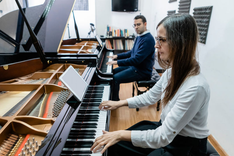 Side view of focused male and female students playing melodies on piano studying in music school