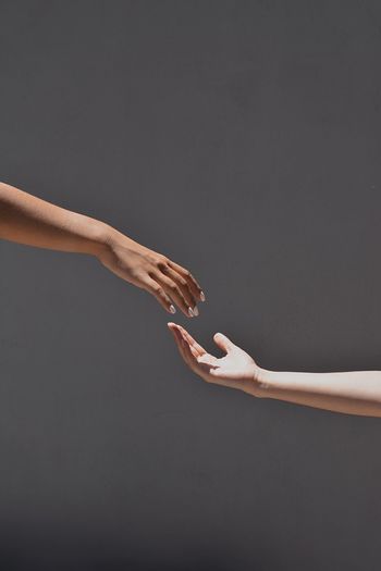 Cropped hands reaching towards each other against gray background