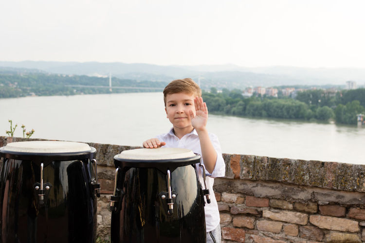 Portrait of boy playing bongo against river