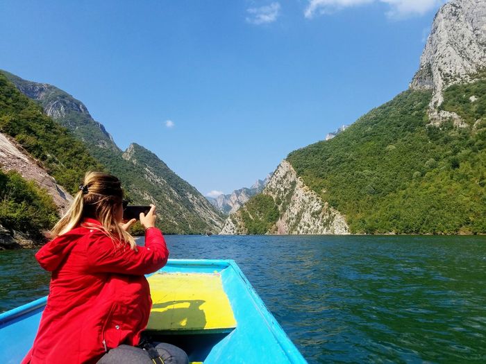 Woman photographing sea while sitting in boat against sky