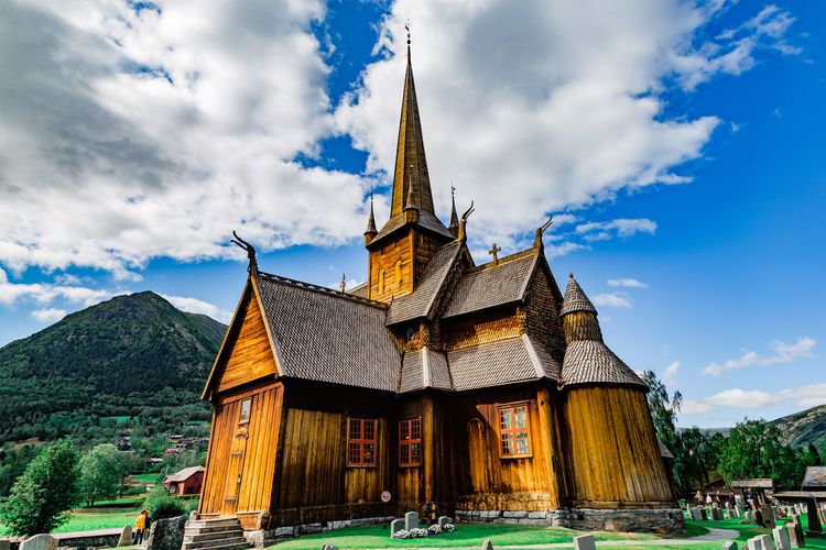 View on the cemetery, medieval stave church in lom, mountains against cloudy sky on a sunny day