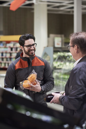 Smiling sales clerk talking man while holding vegetables at supermarket