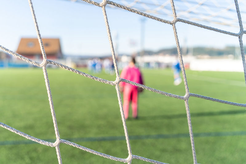 Soccer net in close-up with goalkeeper and other players out of focus on a very sunny day