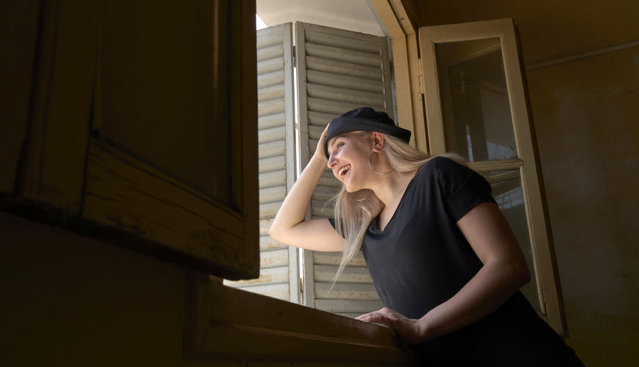 Young woman looking through window at home