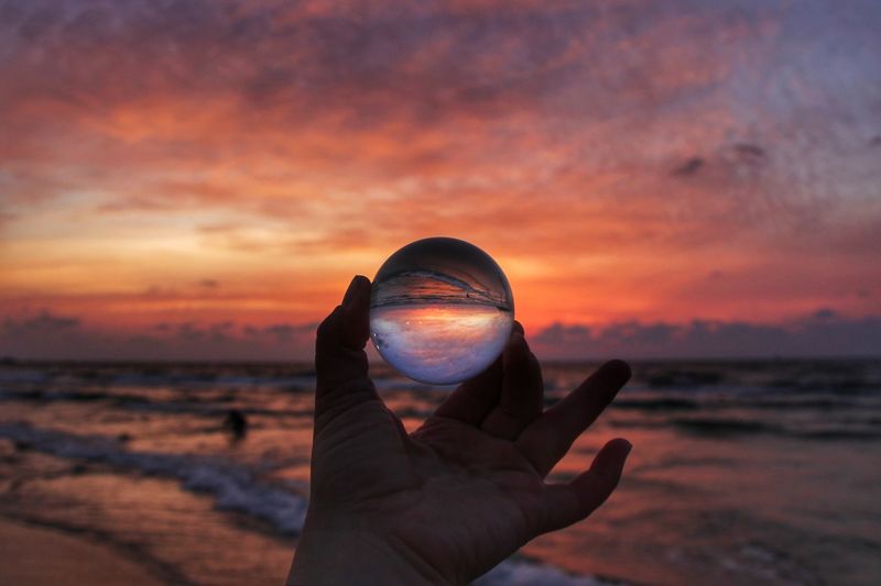 Man holding glass ball at beach during sunset