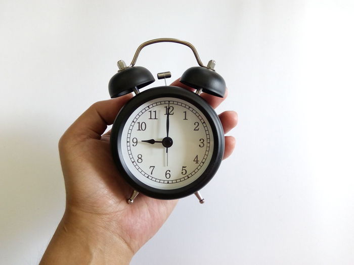 Close-up of hand holding alarm clock against white wall