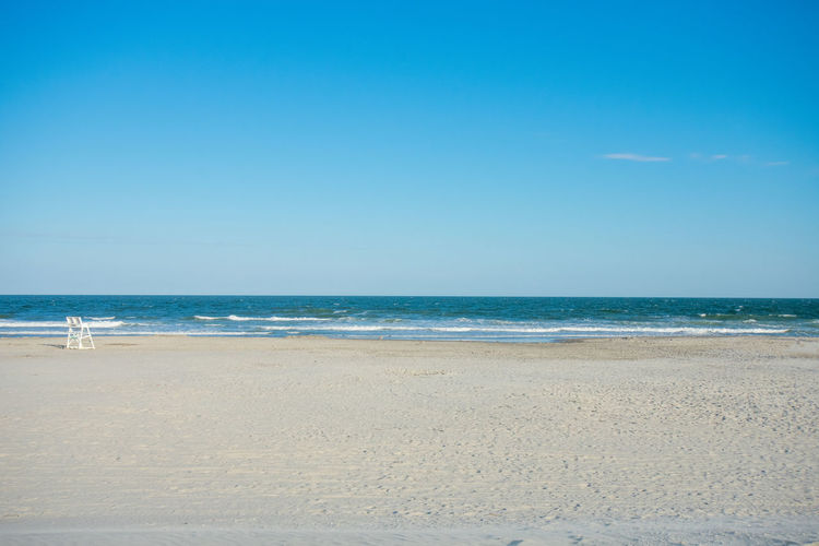 A large empty beach and ocean with a lifeguard chair on a clear blue sky in wildwood new jersey