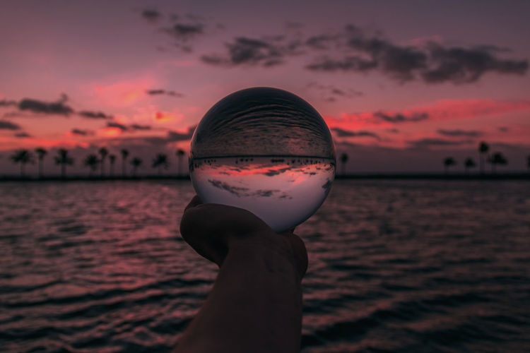 Cropped image of man holding glass ball with upside down sea reflection