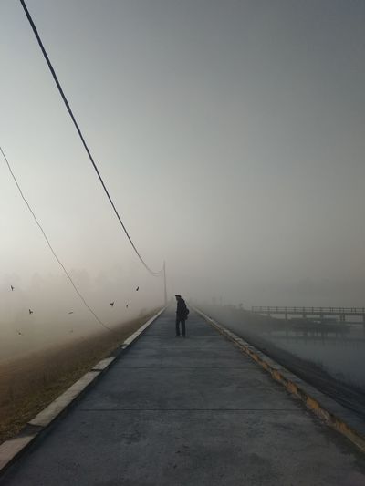 Rear view of person walking on road against sky