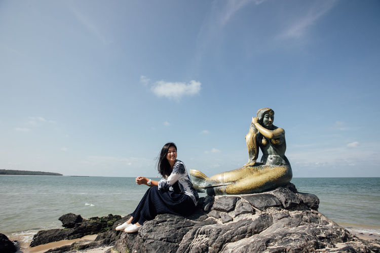 Woman sitting on rock by sea against sky