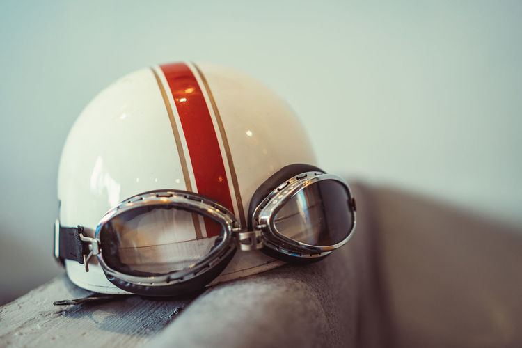Vintage motorbike helmet with goggles placed on back of couch against white wall