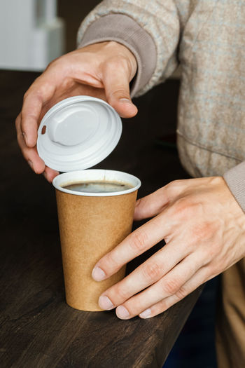 A man bought coffee in a paper cup and closes it with a plastic lid. takeaway food and drink concept