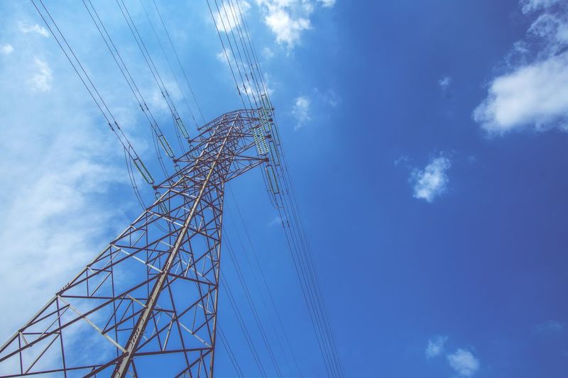 Low angle view of electricity pylon against blue sky