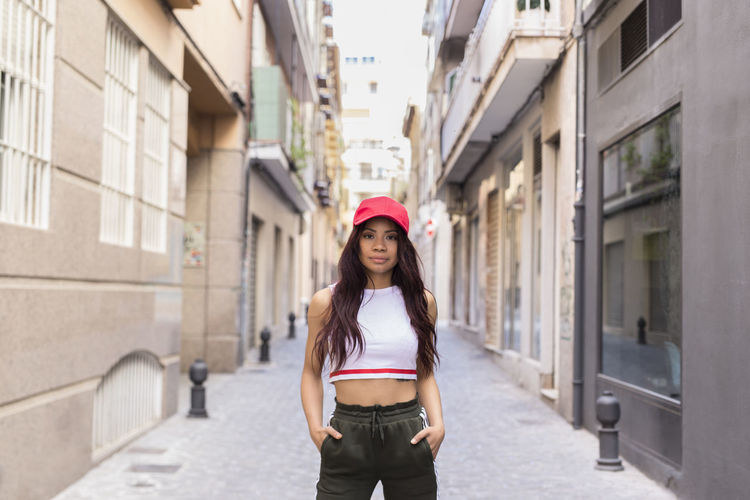 Positive young woman in trendy outfit looking at camera while standing on the city street