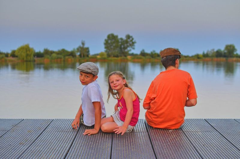 Children sitting on pier. siblings. three children of different age - teenager boy, elementary age