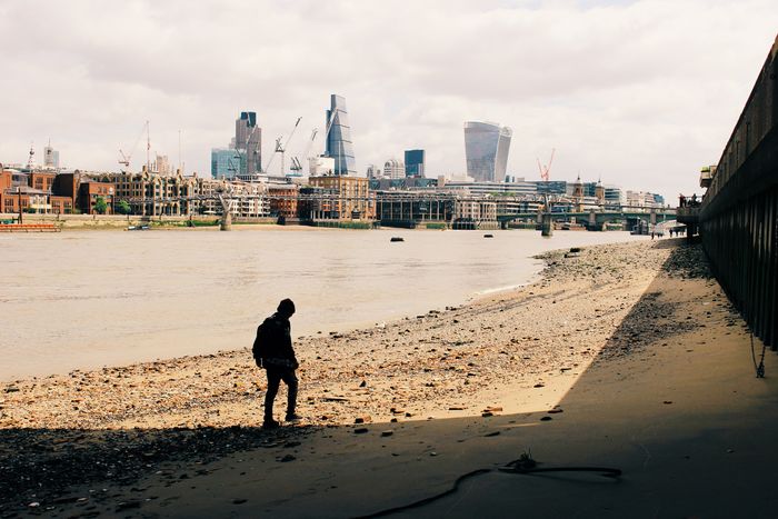 Silhouette man standing on thames riverbank against city